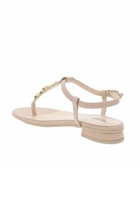Sandalias planas beige con tiras finas, detalles en acento dorado y un pequeño tacón ancho. Material de cuero suave, diseño de punta abierta.