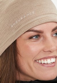 Beige idrottshuvudband med texten "UTHÅLLIGHET." Tillverkat av mjukt, texturerat material, sitter det åtsittande runt huvudet med en slät finish.