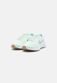 Lys grønn mesh joggesko med hvite aksenter, med en grå swoosh og en teksturert såle. Snørene går gjennom forsterkede snøringer.