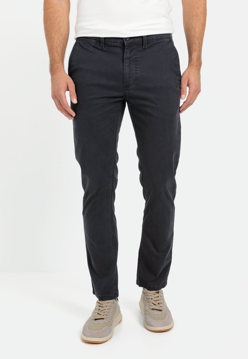 Navyblauwe slim-fit broek met een gladde textuur, een vijf-pocket ontwerp en een enkele knoopsluiting bij de taille. Gecombineerd met lichtgrijze sneakers.