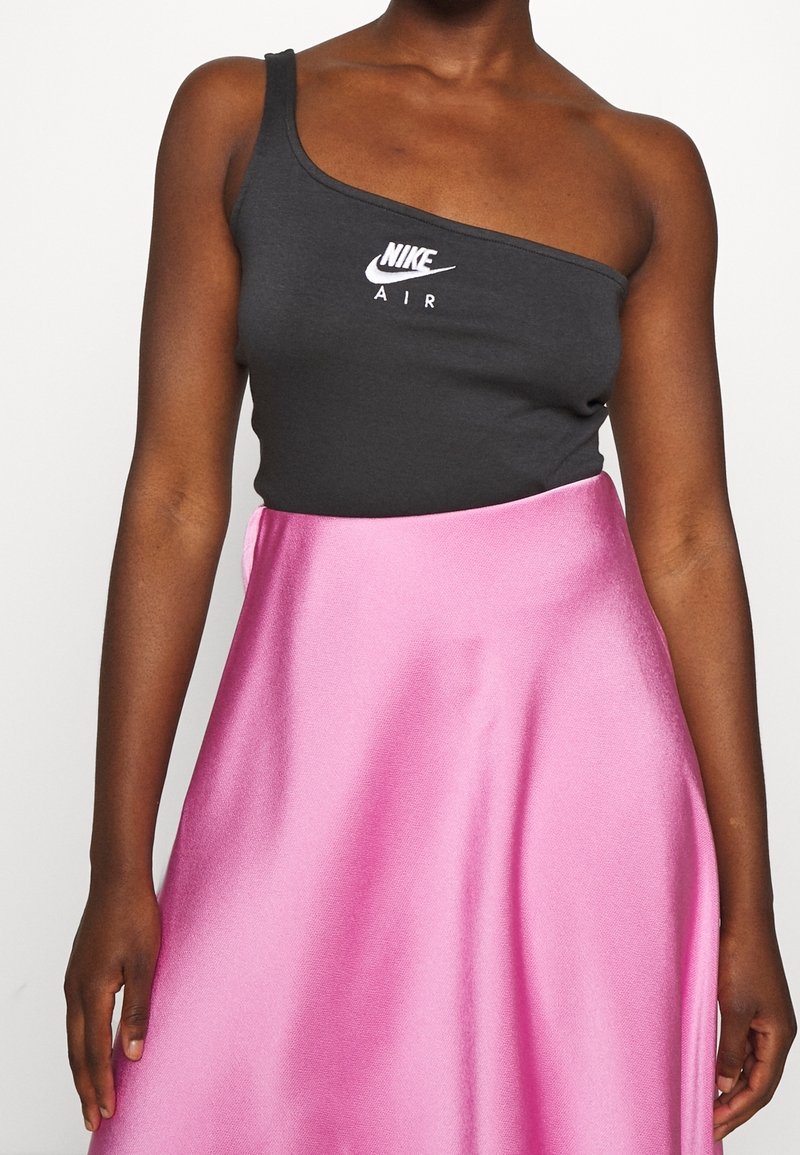 Un débardeur Nike gris à une épaule avec le logo "AIR" en blanc, associé à une jupe en satin fuchsias brillant.