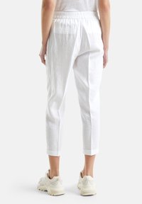 Białe lniane spodnie 3/4 z elastycznym pasem i podwiniętymi mankietami, charakteryzujące się luźnym krojem i delikatną teksturą. Noszone z beżowymi trampkami.