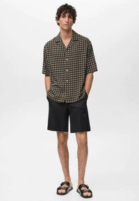 Zwart shirt met korte mouwen en een cirkelvormig patroon, gecombineerd met zwarte shorts en sandalen. Heeft een relaxte fit en lichtgewicht stof.