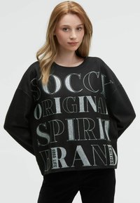 Schwarzer Sweatshirt mit oversized Passform, Rundhalsausschnitt und auffälligem weißen Grafiktext. Das Material hat eine weiche Textur und besteht aus einem gerippten Saumdetail.