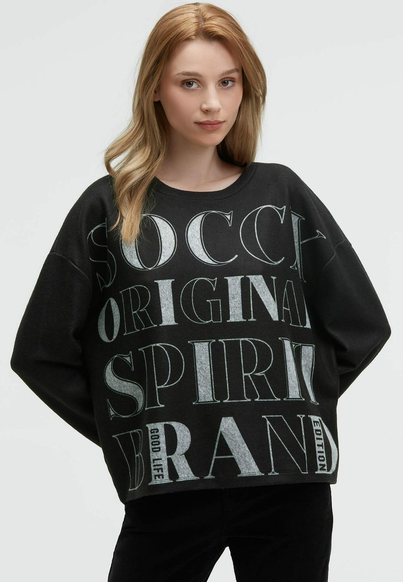 Schwarzer Sweatshirt mit oversized Passform, Rundhalsausschnitt und auffälligem weißen Grafiktext. Das Material hat eine weiche Textur und besteht aus einem gerippten Saumdetail.