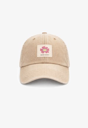 Beige baseballpet met een roze en gele abstracte bloemapplicatie en de tekst "KAOTIKO SOCIETY" in het midden aan de voorkant.