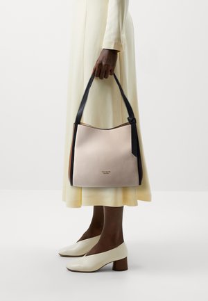 Roze leren handtas met een gebogen vorm en een zwarte riem, met een subtiel logo en een textuur in het oppervlak, gedragen door een persoon in een lichtgekleurde jurk.