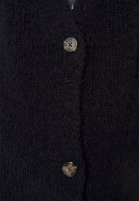 Nahaufnahme von schwarzem gestricktem Stoff mit zwei runden, dunkel marmorierten Knöpfen, die darauf angenäht sind.