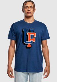 Mørkeblå bomulds-T-shirt med et stort, iøjnefaldende logo i orange og hvid med bogstaverne "U" og "C", der vises tydeligt på fronten.