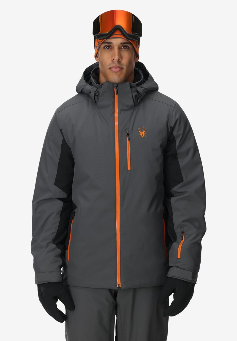Graue Skijacke mit orangefarbenen Akzenten, wasserdichtem Material, verstellbarer Kapuze, Reißverschluss-Taschen und Logo auf der Brust. Schwarze Ärmelabschnitte.