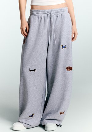 Wide gray sweatpants with small embroidered dachshund dogs in various colors worn with white shoes and a cropped white top.