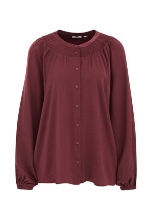 Blouse à manches longues bordeaux avec un col rond, des détails froncés au niveau de la poitrine et une fermeture à boutons sur le devant. Tissu doux et léger avec une finition texturée.