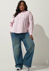 Ljust rosa och vit randig långärmad skjorta med knappar, ihopparat med lösa blå denimjeans och vita sneakers.