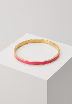 Bracelet jonc fin en or avec incrustation d'émail rose vif reposant sur un socle cubique blanc, sur un fond gris clair.