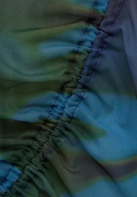 Gros plan d’un tissu froncé avec une couture froncée, montrant des dégradés de bleu, vert et noir et un matériau texturé semblable à un mesh.