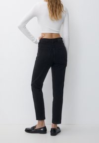 Jeans negros de cintura alta con piernas ajustadas, que presentan dos bolsillos traseros y una tela texturizada, combinados con mocasines negros.