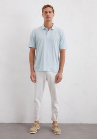 Lichtblauwe polo met korte mouwen, met knoopkraag; gecombineerd met witte opgerolde broeken en beige veterschoenen. Eenvoudig, casual ontwerp.