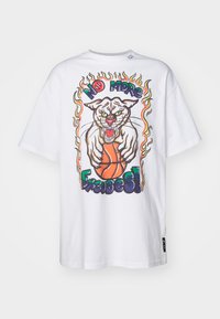 Biela bavlnená tričko s veľkým grafickým dizajnom syčiaceho mačky, ktorá drží basketbal, obklopená farebnými plameňmi a výrazným textom.