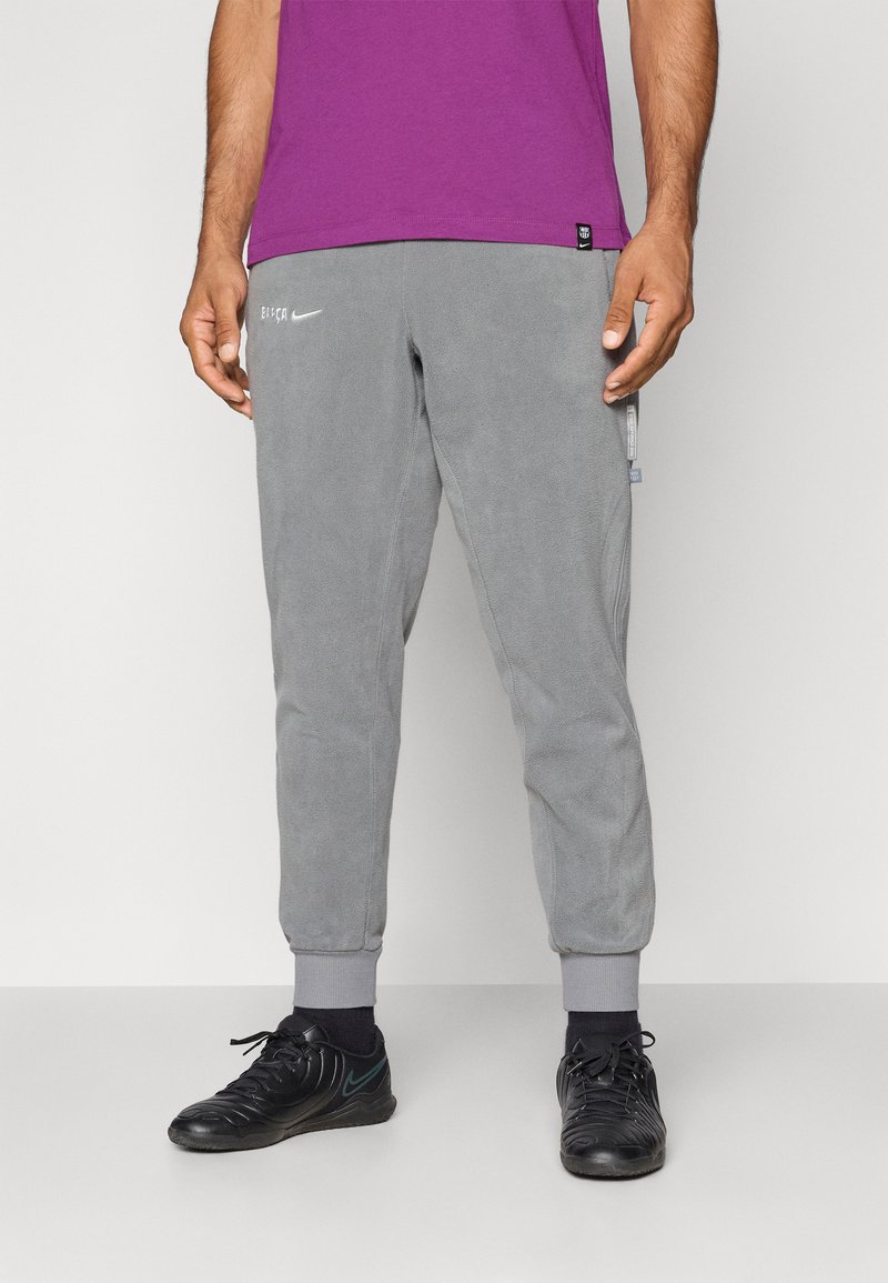 Sive flis hlače s tapered manšetami, ki imajo majhen bel logotip in stransko žep. Usklajene z črnimi supergami in vijolično majico.