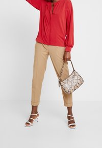 Camicia rossa a maniche lunghe, pantaloni beige su misura, sandali con tacco bianchi e a strappo, e una borsa in stampa pitone beige. Caratteristiche di design equilibrato e elegante.