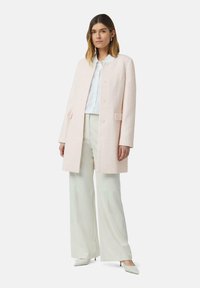 Lichtroze textuurjack met een rechte snit, knopen aan de voorkant en twee zakken, gecombineerd met een witte blouse en crèmekleurige wijde broek.
