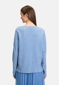 Helles blaues Wollpullover mit lässiger Passform, weitem Ausschnitt und langen Ärmeln, kombiniert mit einem plissierten blauen Rock. Weiche Textur, minimales Design.