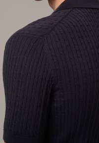 Polo shirt en tricot bleu marine avec un motif en câble texturé, manches courtes et un col classique. Fini en tissu lisse.