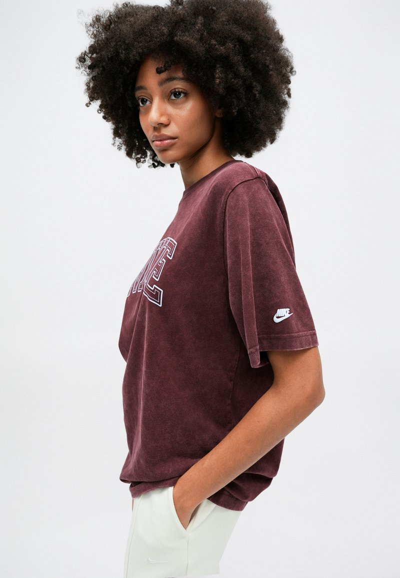 Bordeaux rotes Oversize-T-Shirt mit kurzen Ärmeln, einer weißen gestickten Schrift und einem kleinen Nike-Logo am linken Ärmel. Weicher Stoff.