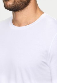 T-shirt bianca in cotone con scollatura rotonda e maniche corte, caratterizzata da una texture liscia e un design minimalista.