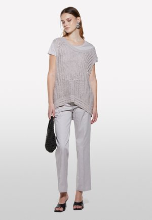 Top en tricot gris clair à coupe ample, superposé à un t-shirt à manches courtes ; associé à un pantalon clair ajusté et des sandales à talons carrés noires.