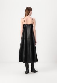 Schwarzes Lederkleid mit dünnen Trägern, das eine fließende Silhouette und glatte Textur aufweist und bis zur Mitte der Waden reicht.