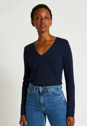Haut à manches longues en v navy en tissu lisse, associé à un jean bleu taille haute avec une fermeture classique à boutons et à glissière.