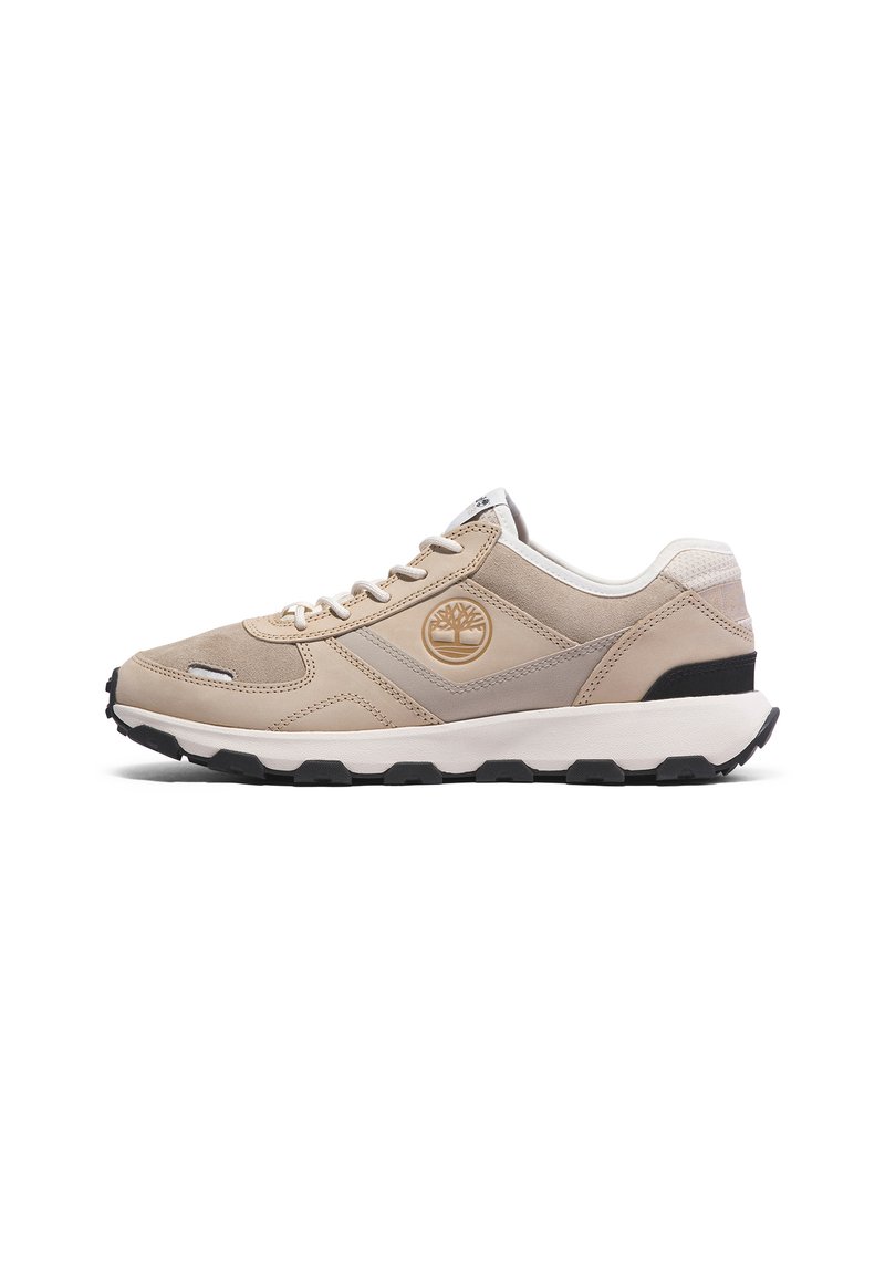 Beżowe buty sportowe z teksturowanym zamszowym cholewką, białymi akcentami, czarną gumową podeszwą oraz okrągłym logo po boku.