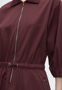 Σκούρο κόκκινο μπουφάν με φερμουάρ μπροστά, ελαστική μέση με κορδόνι και ελαστικές μανσέτες σε μανίκια τριών τετάρτων.