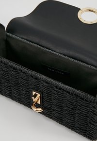 Sac à main noir tissé avec un extérieur texturé, des embellissements en or et un intérieur noir lisse. Dispose d'un fermoir à clasp et d'une étiquette intérieure.