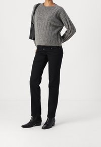 Persona vistiendo un suéter gris de punto trenzado, pantalones negros rectos, botas negras de tobillo y llevando un bolso negro de hombro.
