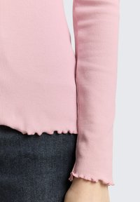 Różowy prążkowany top z długim rękawem z falowanym wykończeniem na dole i mankietach, wykonany z miękkiego materiału, zestawiony z ciemnym denimu.