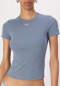 Short-sleeved, fitted ribbed t-shirt in soft blue fabric with a small red logo on the chest. Seamless round neckline, midriff length.