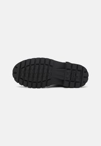 Semelle de chaussure en caoutchouc noir avec des rainures profondes et le nom de la marque BOSS embossé près du talon.