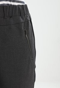 Calças cinza-escuras com uma cintura elástica, apresentando um bolso lateral com zíper e um tecido liso e texturizado.