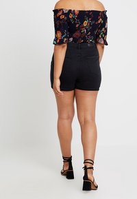 Pantalones cortos negros de talle alto con un diseño ajustado, combinados con una blusa negra de flores, sin hombros, con mangas con volantes y colores vibrantes.