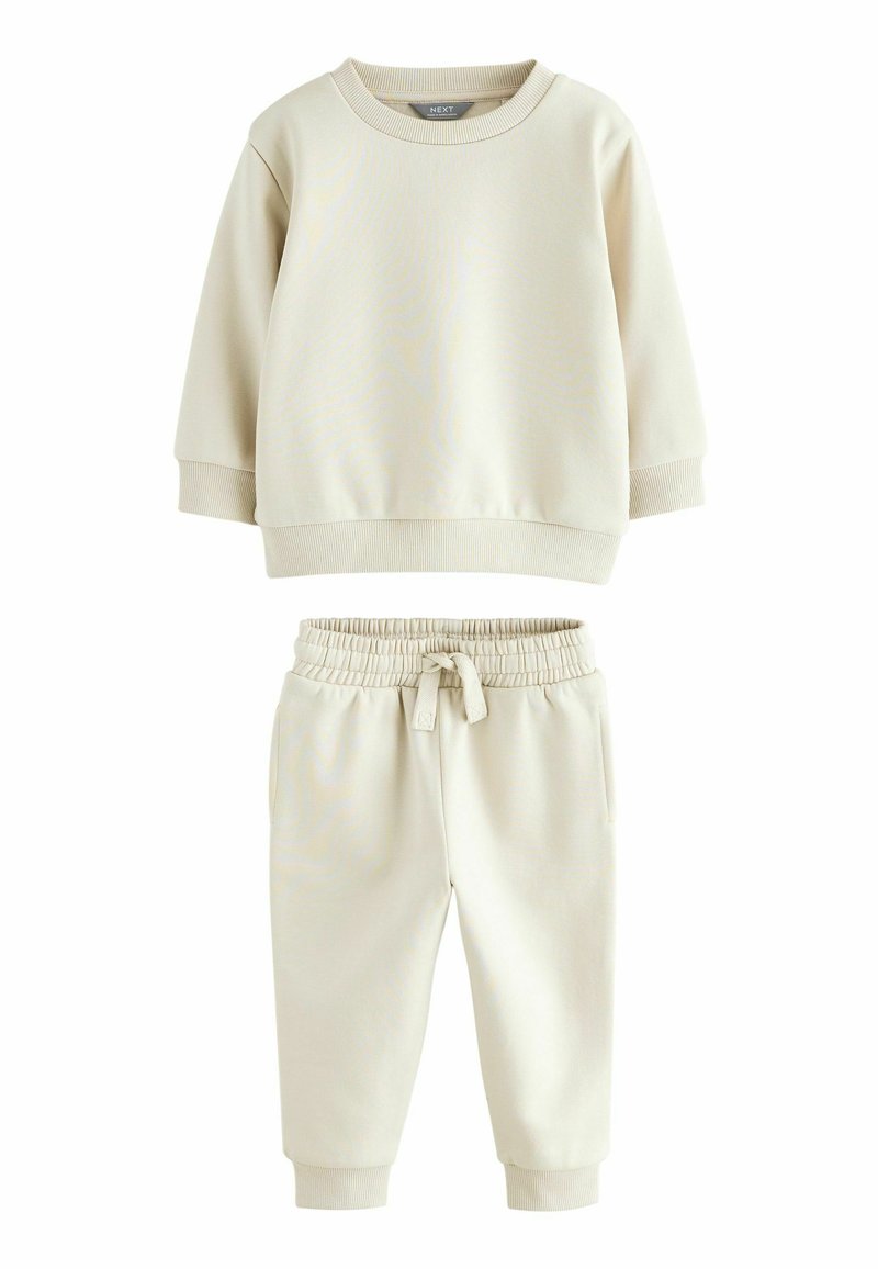 Sudadera de algodón color crema y pantalones de chándal a juego. La sudadera tiene un cuello redondo y puños acanalados; los pantalones tienen una cinturilla elástica.