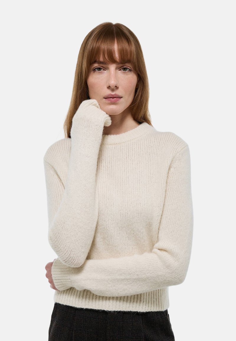 Pull en tricot couleur crème avec une texture côtelée, un col rond et des manches longues. Le tissu a l'air doux et confortable.