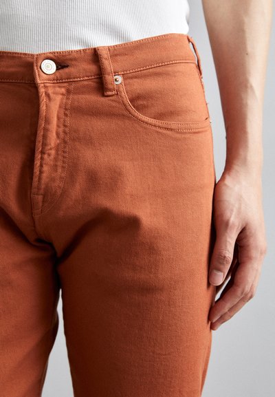 Rostfärgade denimjeans med en slät textur, femficksdesign, metallknappknäppning och synlig sömsdetalj.