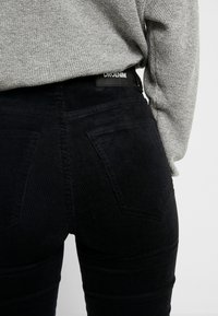 Svarta kordjeans med en texturerad yta, med en figurnära design och bakfickor, i kombination med en ljusgrå stickad tröja.