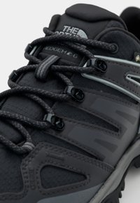 Grå vandresko med tekstureret syntetisk overdel, reflekterende detaljer og slidstærk gummisål. Snørebåndsdesign med sorte hardware og logo detaljer.