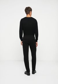 Schwarzer gerippter Pullover mit langen Ärmeln, kombiniert mit schwarzen schmal geschnittenen Hosen. Das Outfit zeichnet sich durch ein schlichtes Design und eine figurnahe Silhouette aus.