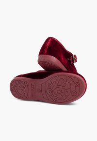 Zapatos slip-on de terciopelo rojo con punta redondeada y un detalle de hebilla lateral, con una suela de goma texturizada decorada con patrones de corazones y flores.