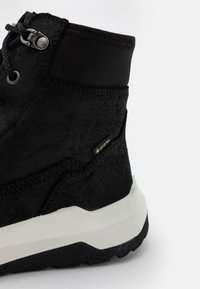 Stivale nero impermeabile con parte superiore testurizzata e collare imbottito, dotato di una suola intermedia bianca e un'etichetta GORE-TEX sul lato.