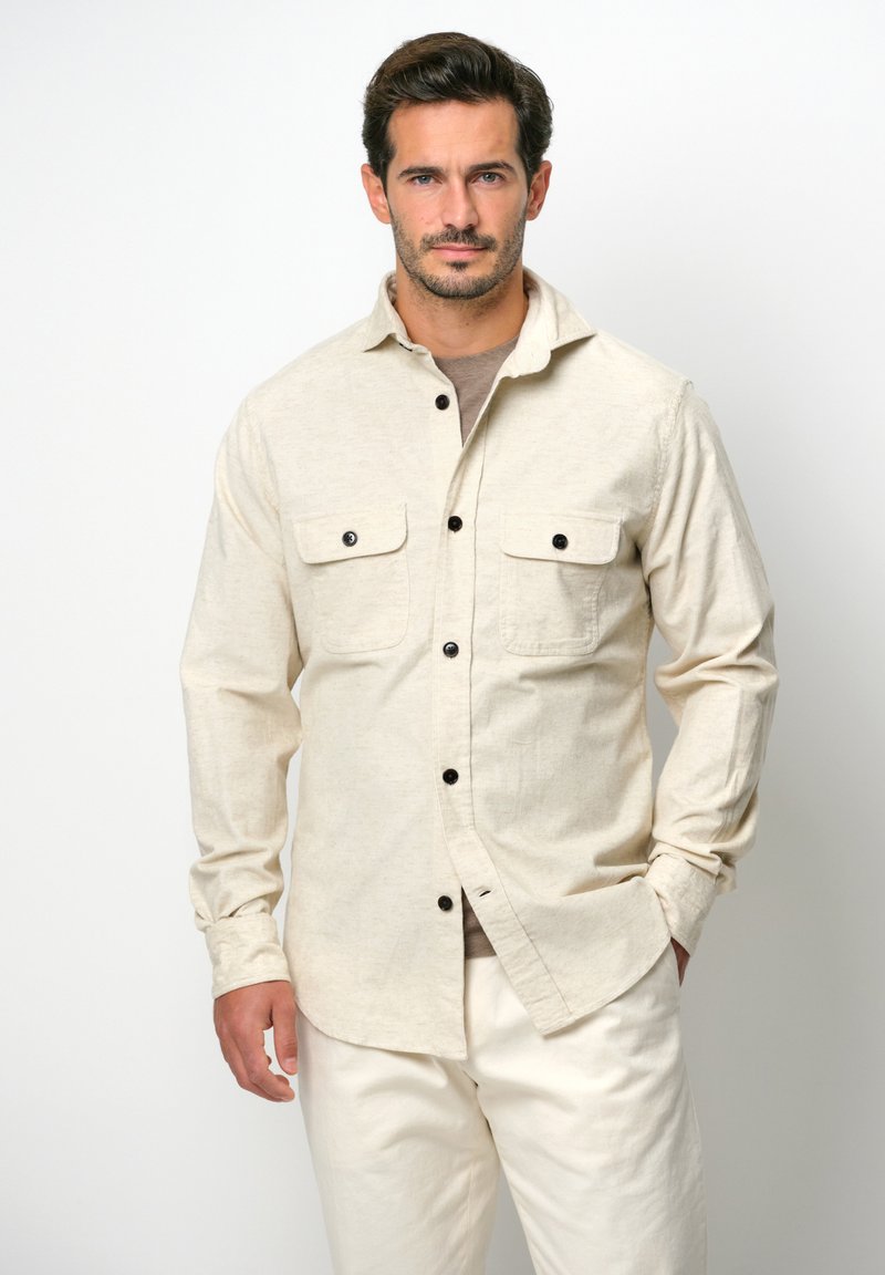 Lichtbeige button-up shirt met twee borstzakken, zwarte knopen en een zachte textuur, gecombineerd met lichtcrème broeken.